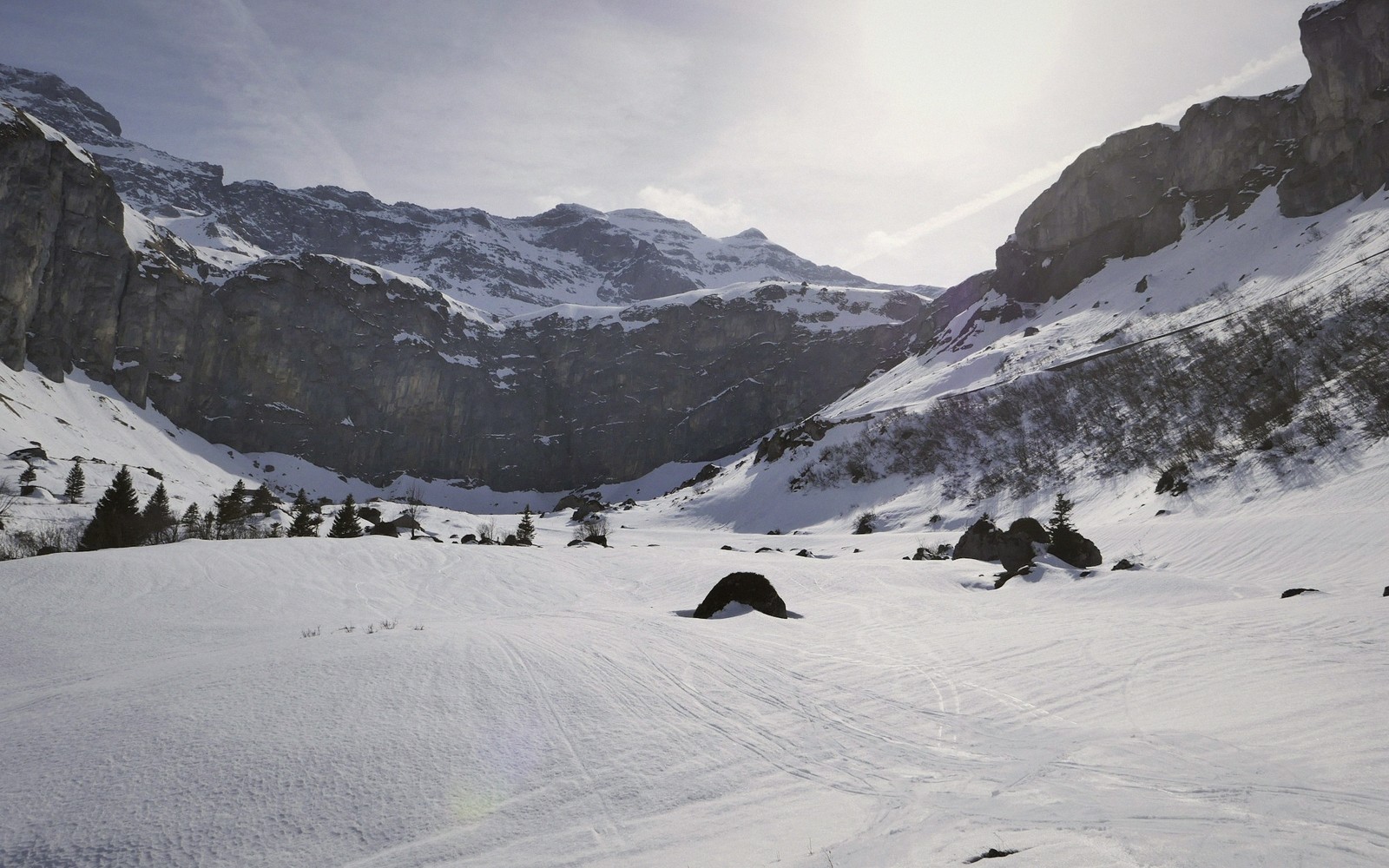 A sunlit red run with a lone distant skier, the resort below