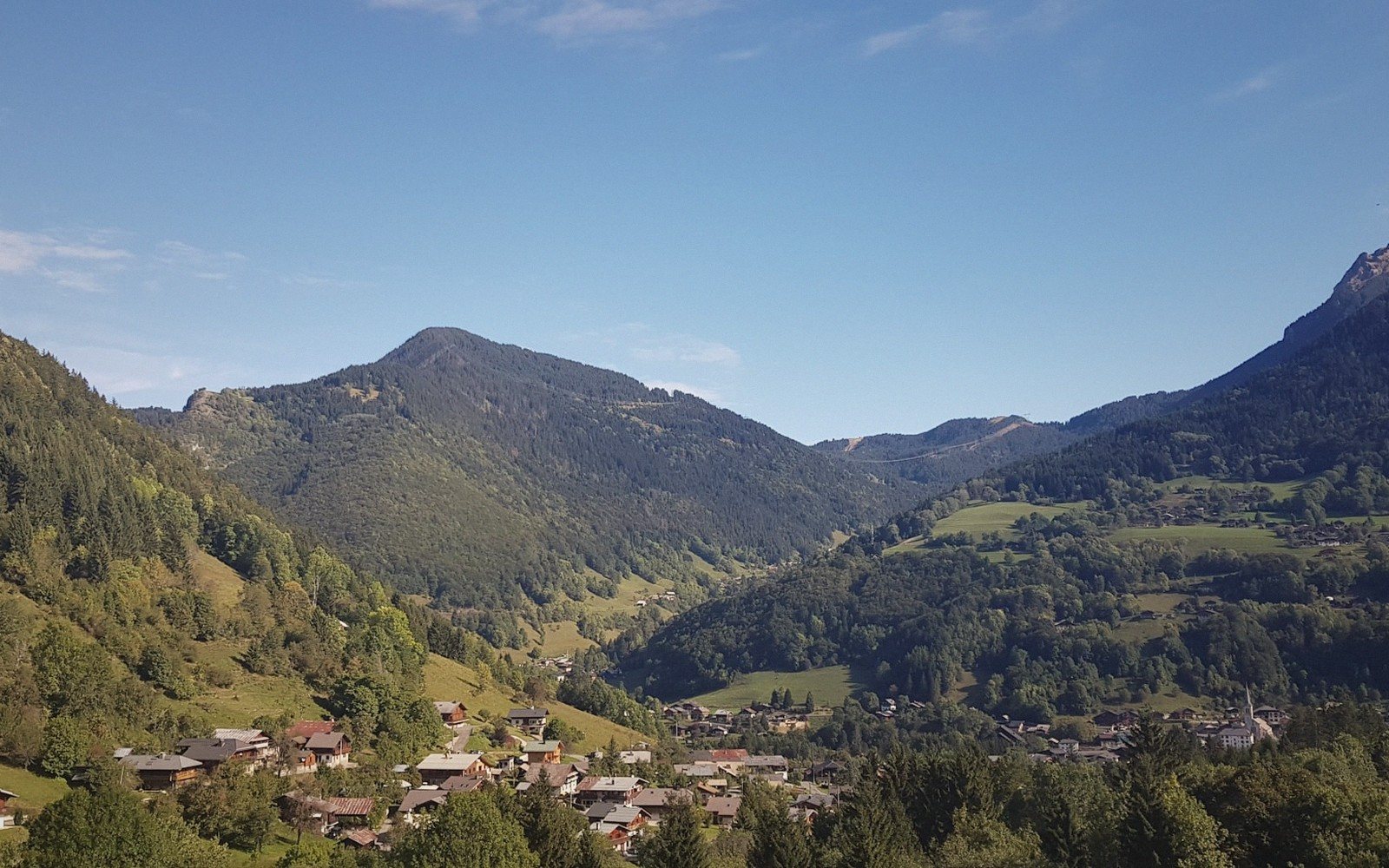 The Maurienne below — stone hamlets, larch forest, and the road over the pass.
